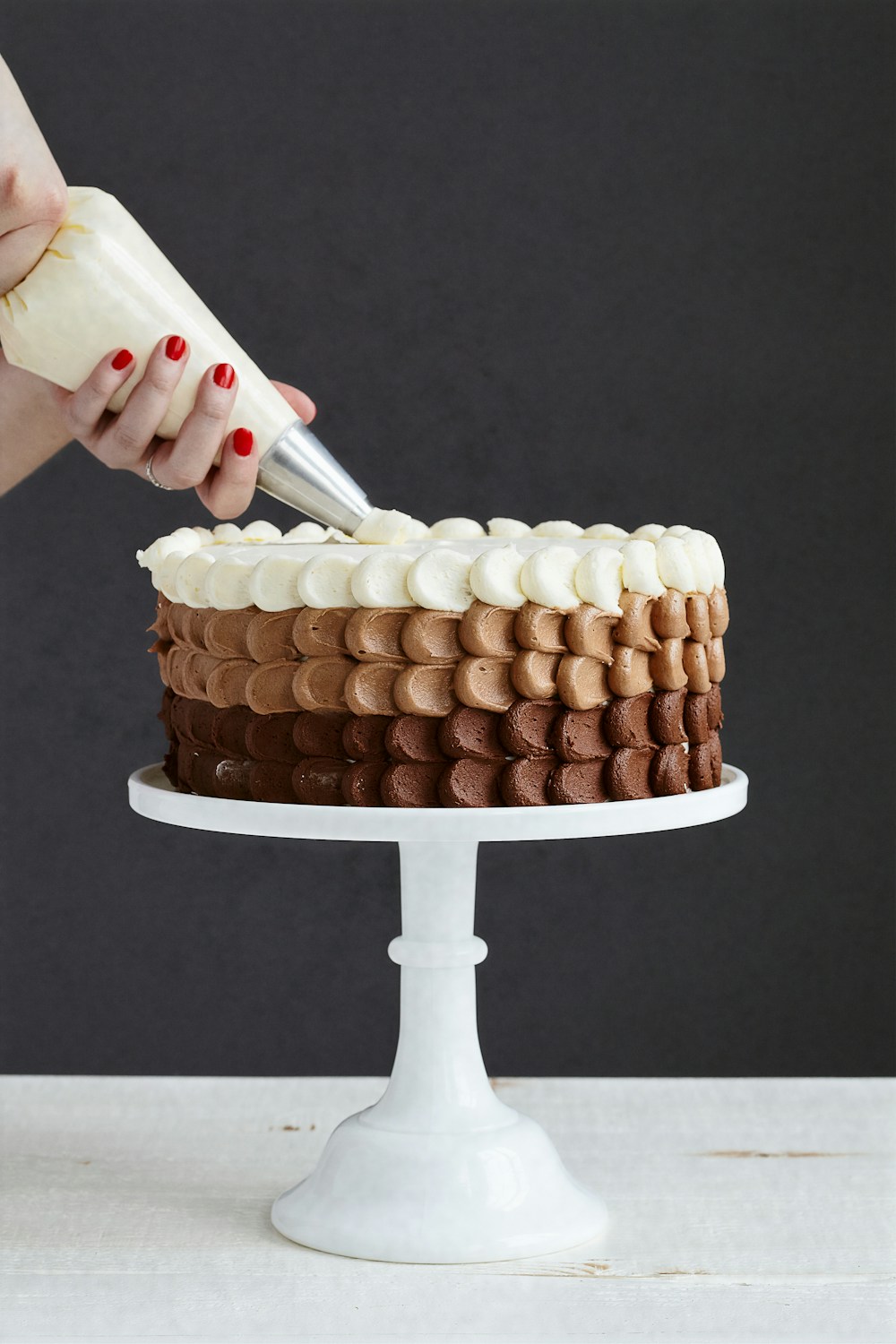 Hands decorating cake with pink buttercream rose
